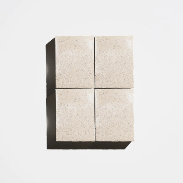 Four square natural beige soap bars arranged in a 2x2 grid on a light background