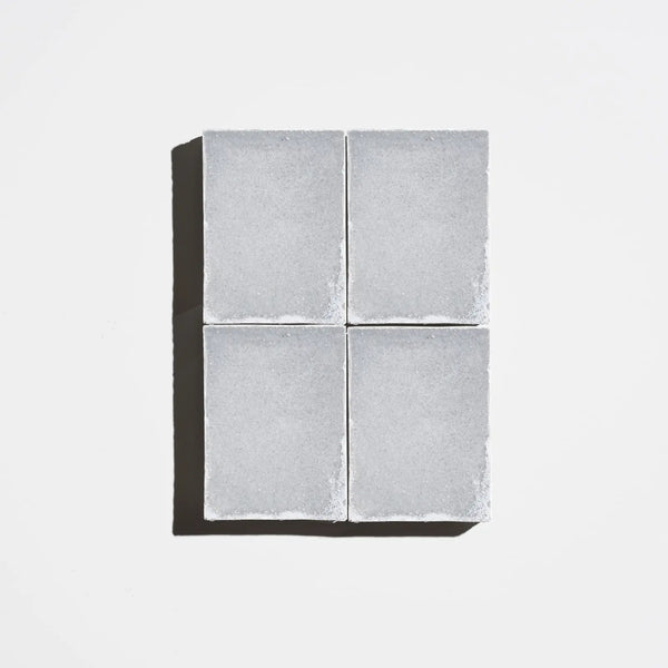Four square charcoal-gray natural soap bars arranged in a 2x2 grid on a light background