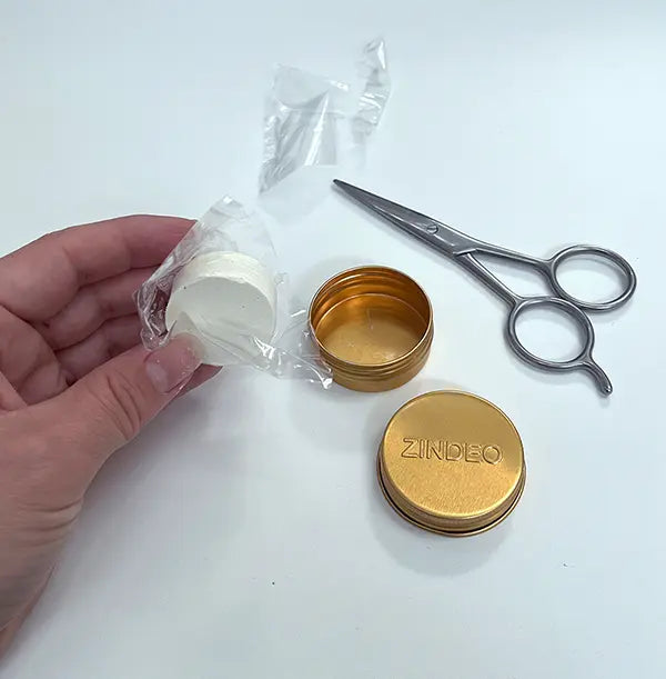 Mão a desembrulhar uma recarga de Anti-odorant Cream ZINDEO ao lado de uma lata dourada aberta